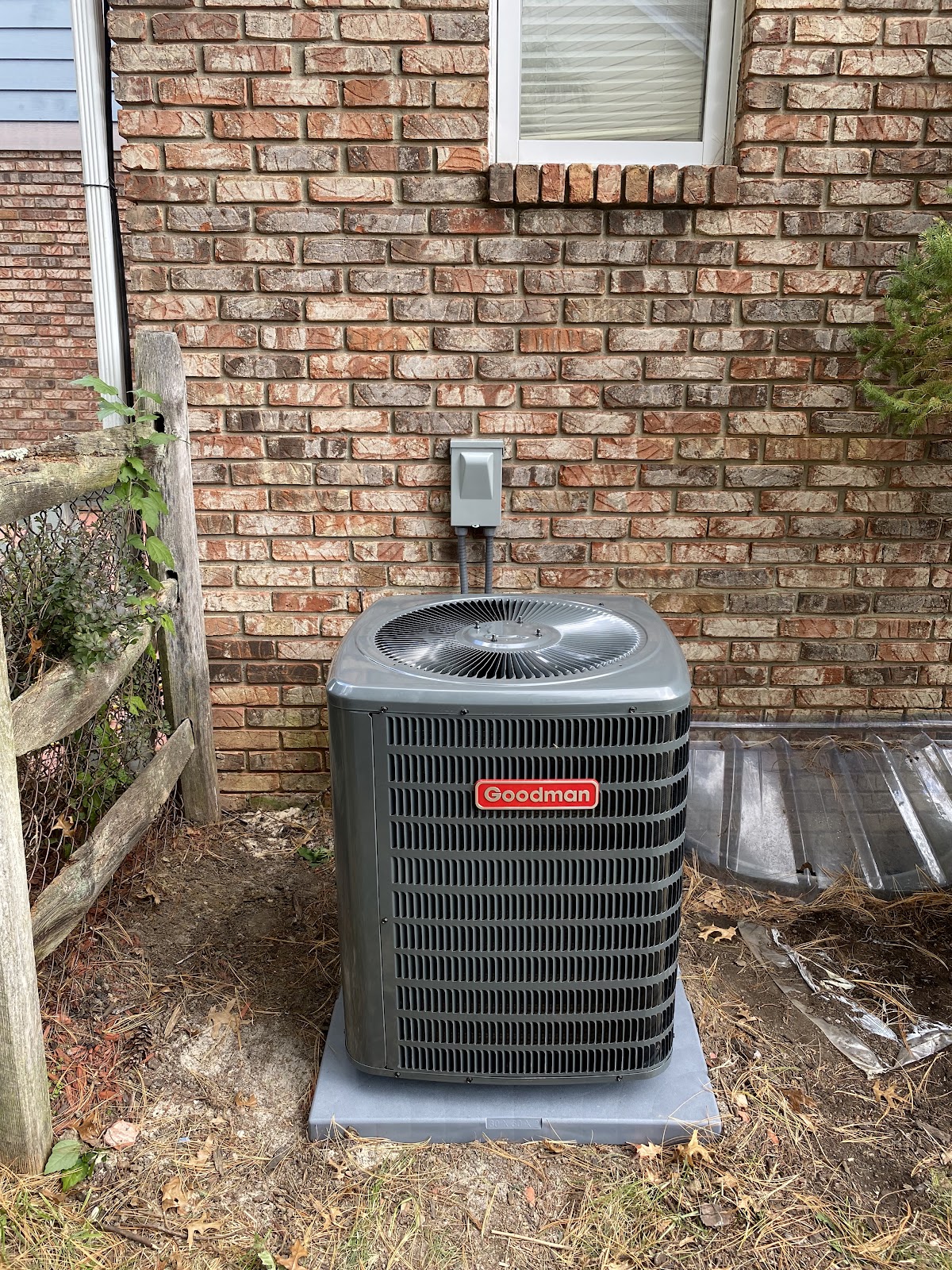 Newly installed Goodman central air conditioning condenser against a brick home exterior