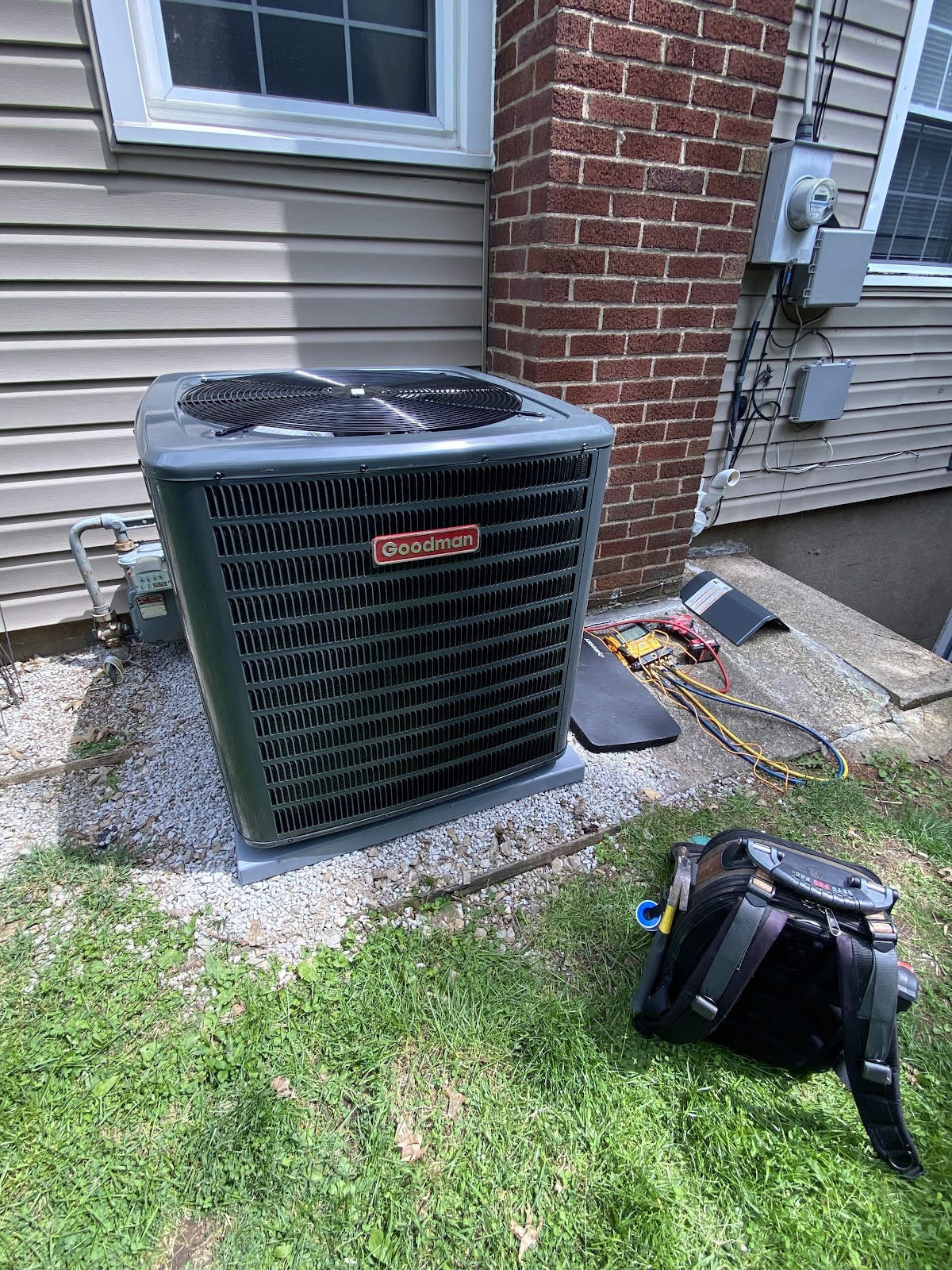 Goodman central air conditioning condenser installed against vinyl siding with a gas meter and electrical panel nearby